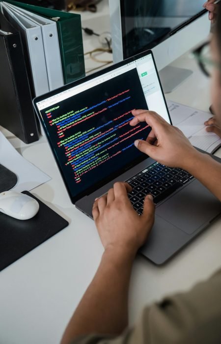 pexels-photo-12899188-12899188 Close-up of a programmer pointing at a colorful code script on a laptop in an office setting.